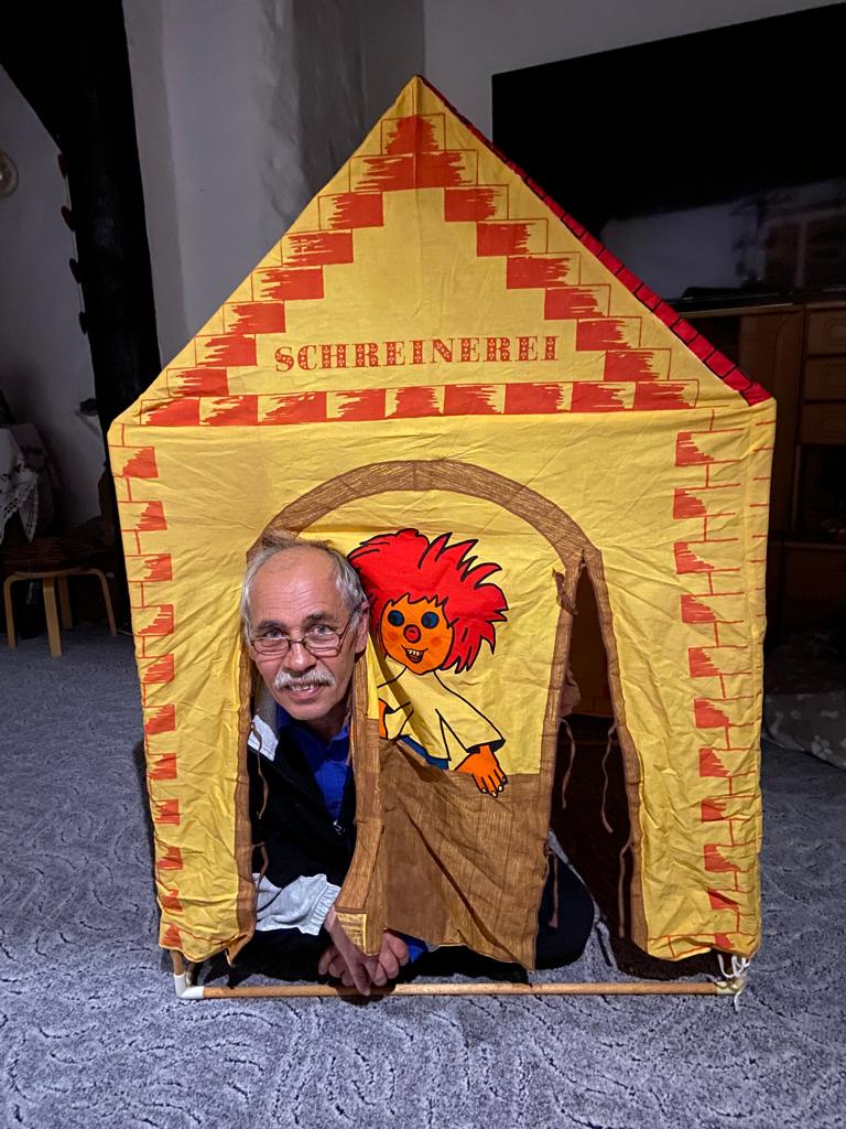 Sven Coorßen schaut aus der offene Tür eines Kinderzelt von der Marke Sioux Sheriff Esber. Auf dem Kinderzelt steht Schreinerei und es gibt ein Motiv des Pumuckls.